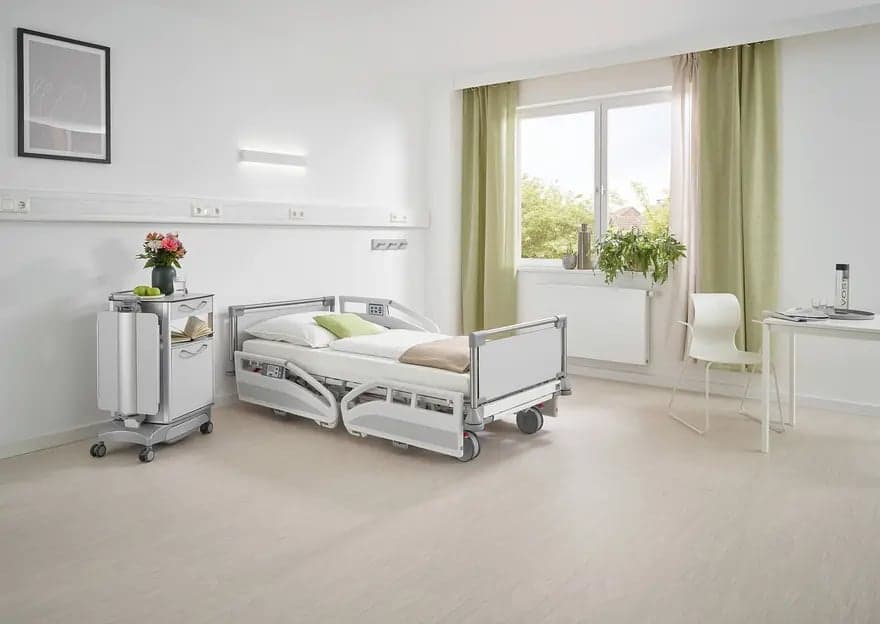 Cama hospitalar Evario em quarto de internação claro, com mesa de cabeceira Quado
