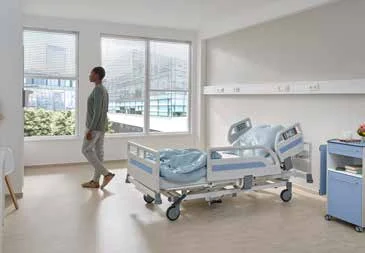 Fase 4 da mobilização precoce: paciente caminhando sozinho pelo quarto de internação, com o leito hospitalar Stiegelmeyer vazio ao fundo